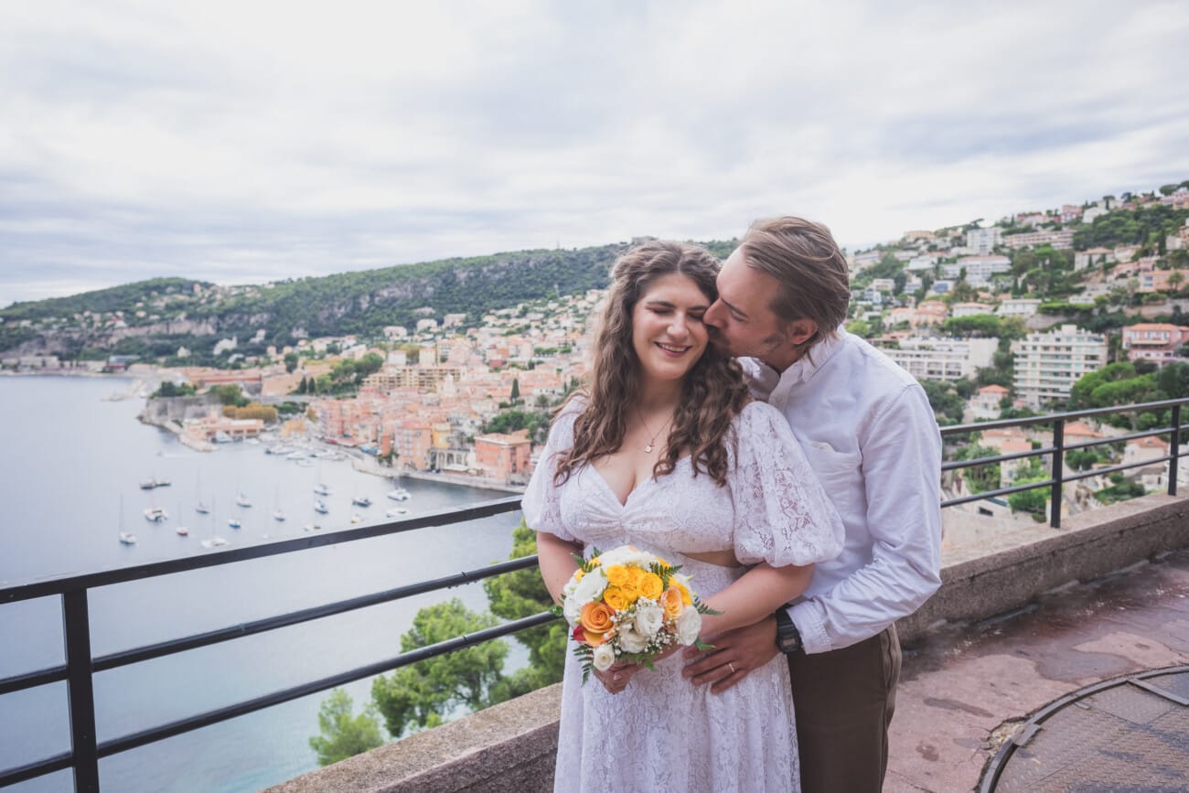 Tender elopement kiss on French Riviera, with Villefranche-sur-Mer town and seaside in the backdrop
