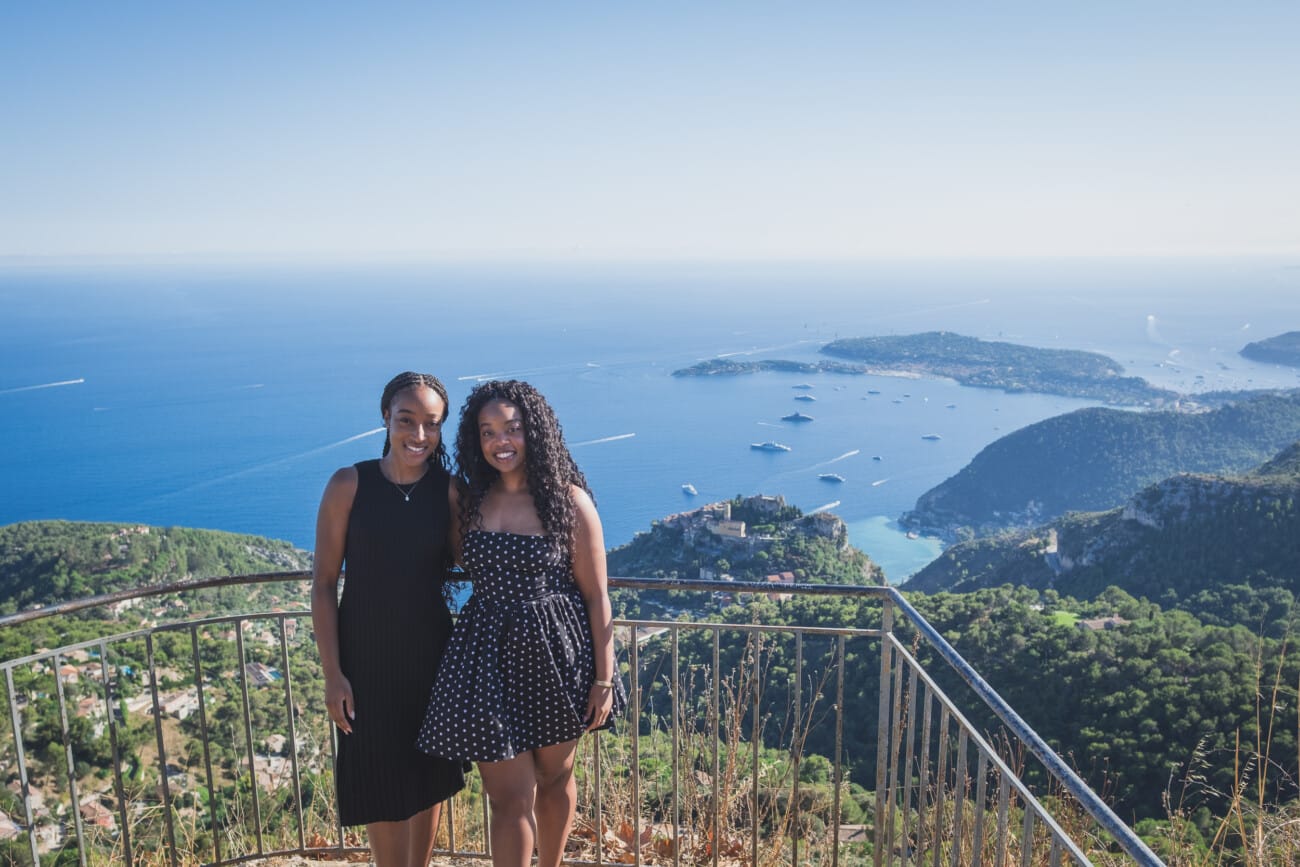 The Ultimate Girls’ Trip: A Mother and Daughters’ Legacy Session on the French Riviera 5 The two sisters standing back-to-back overlooking the blue waters of the Riviera, capturing lifelong family memories.