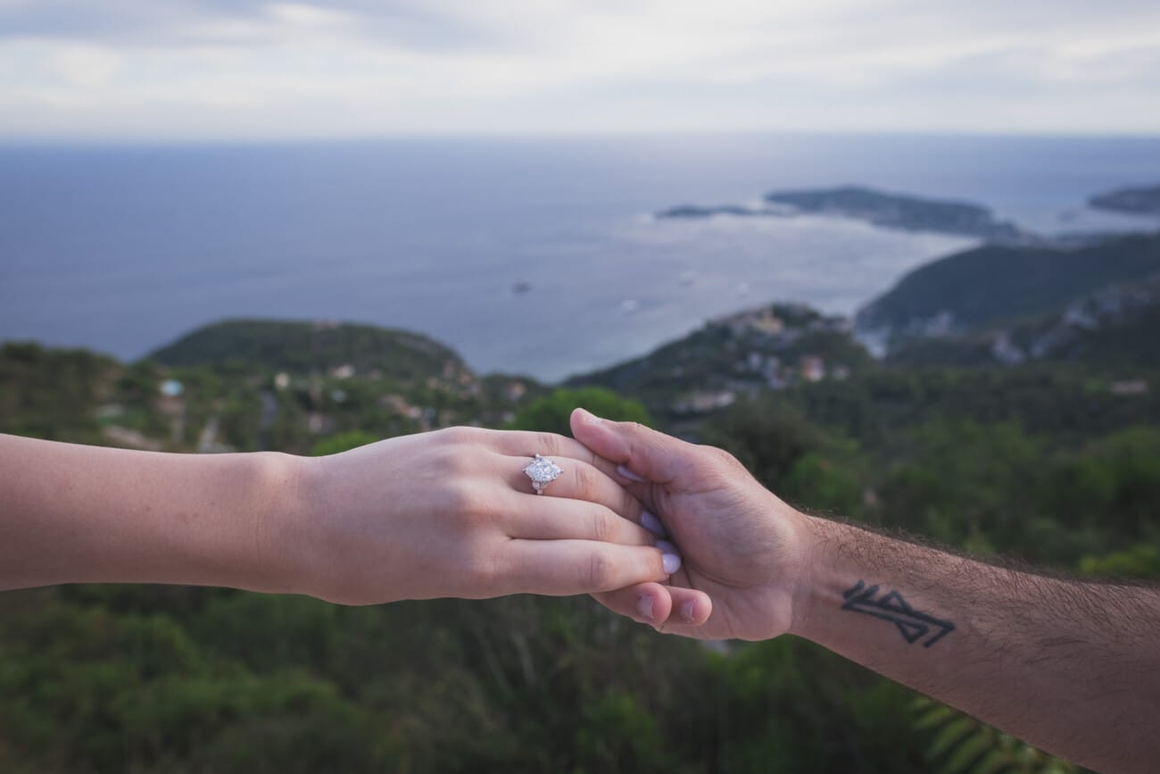 Close up detail of the engagement ring on her finger with the blue ocean in the background.